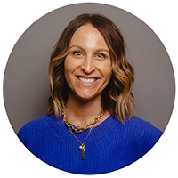 A woman wearing a blue sweater smiles warmly.
